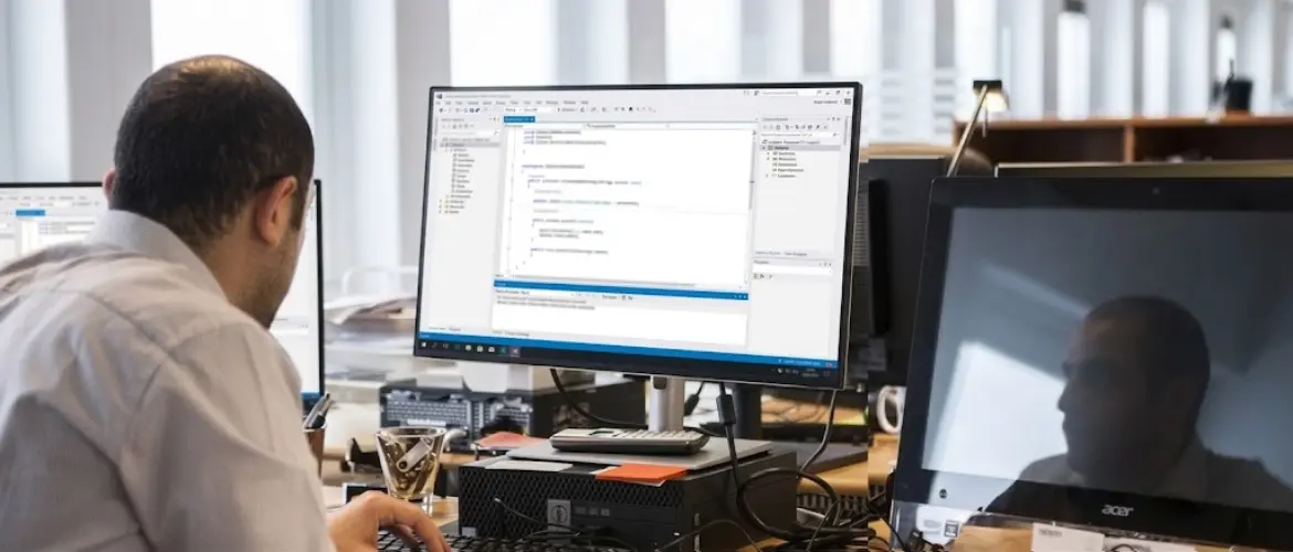 Software developer working at a desk with multiple monitors displaying programming code.